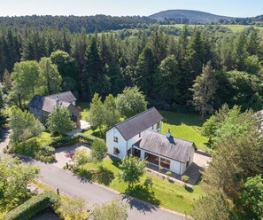 Ett bostadsområde med två hus omgivna av tät skog, en klar himmel och ett kuperat landskap i bakgrunden.