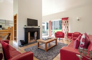 Un salon avec une cheminée, des canapés rouges, une table basse en bois et un téléviseur fixé au-dessus de la cheminée.