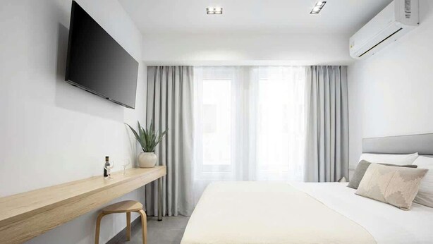 Ein Hotelzimmer mit Bett, Wandfernseher, Schreibtisch mit Stuhl und einer Zimmerpflanze.