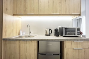 Cozinha moderna com armários de madeira, pia de aço inoxidável, máquina de café, micro-ondas e lava-louças.