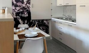 Eine moderne Küche mit weißen Schränken, einem Esstisch mit Tellern, Gläsern und Besteck sowie einem Stuhl.