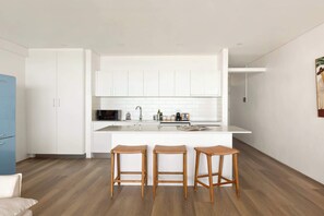 Una cocina moderna con armarios blancos, una isla central y tres taburetes de madera.