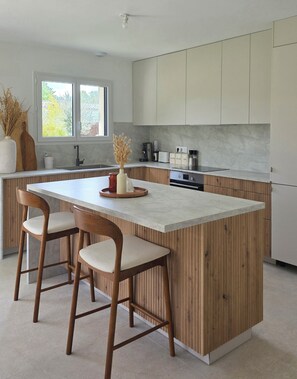 A modern kitchen with a central island, wooden accents, and a view of the outdoors. - Summer villa. - Illuminated garden & Brazier (Lesparre-Médoc)
