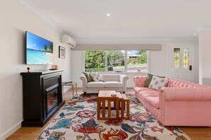 A living room with a fireplace, a television, a sofa, a pink couch, and a patterned rug. - Garden Retreat 2-Bed House Wentworth Falls (Wentworth Falls)