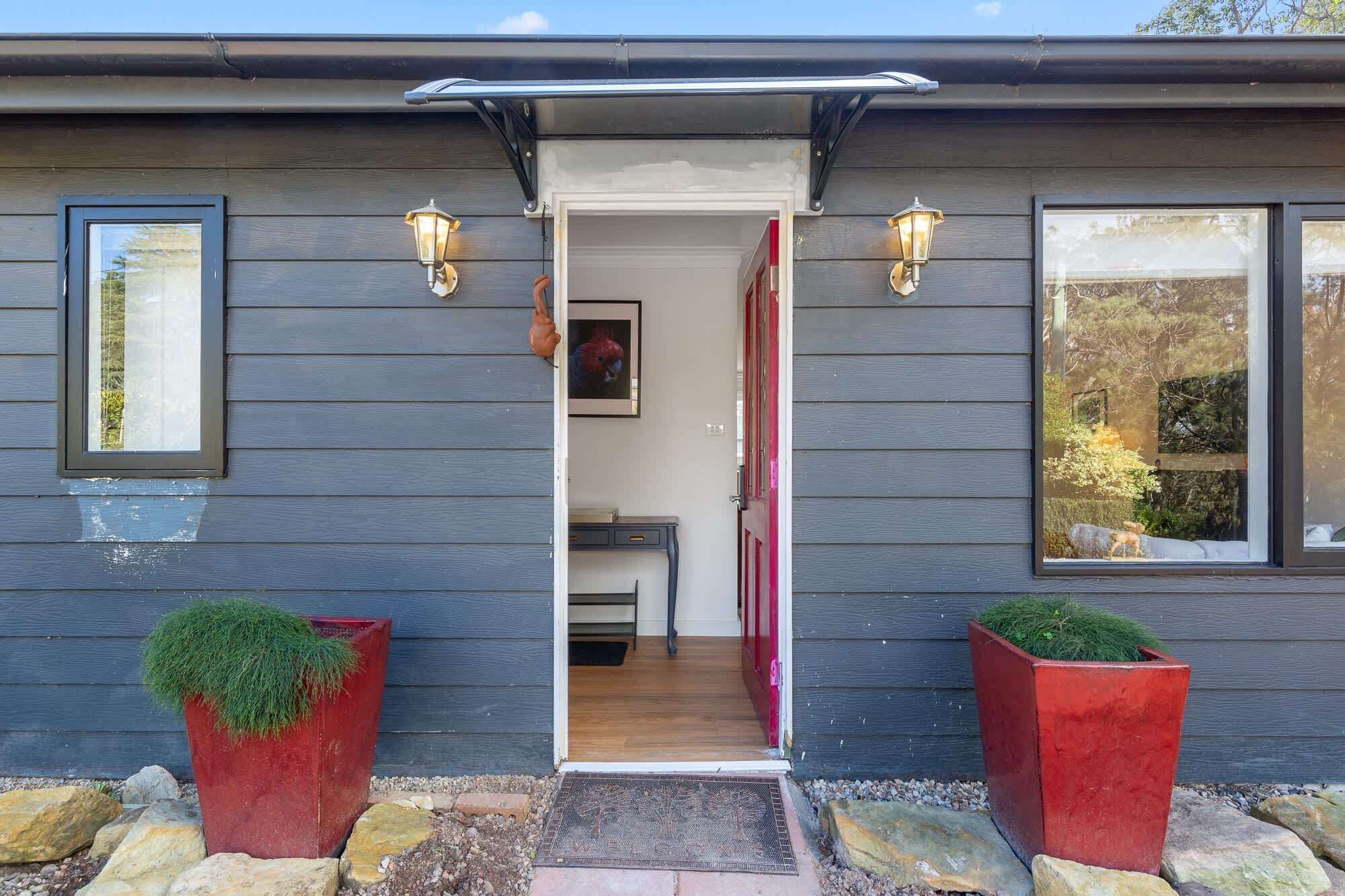 A house entrance with a door, two wall-mounted lights, and two potted plants.
