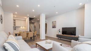 A modern living room with a sofa, coffee table, TV, and a dining area with chairs and a table. - Apartamentos Dúplex Príncipe de Canalejas (Madrid)