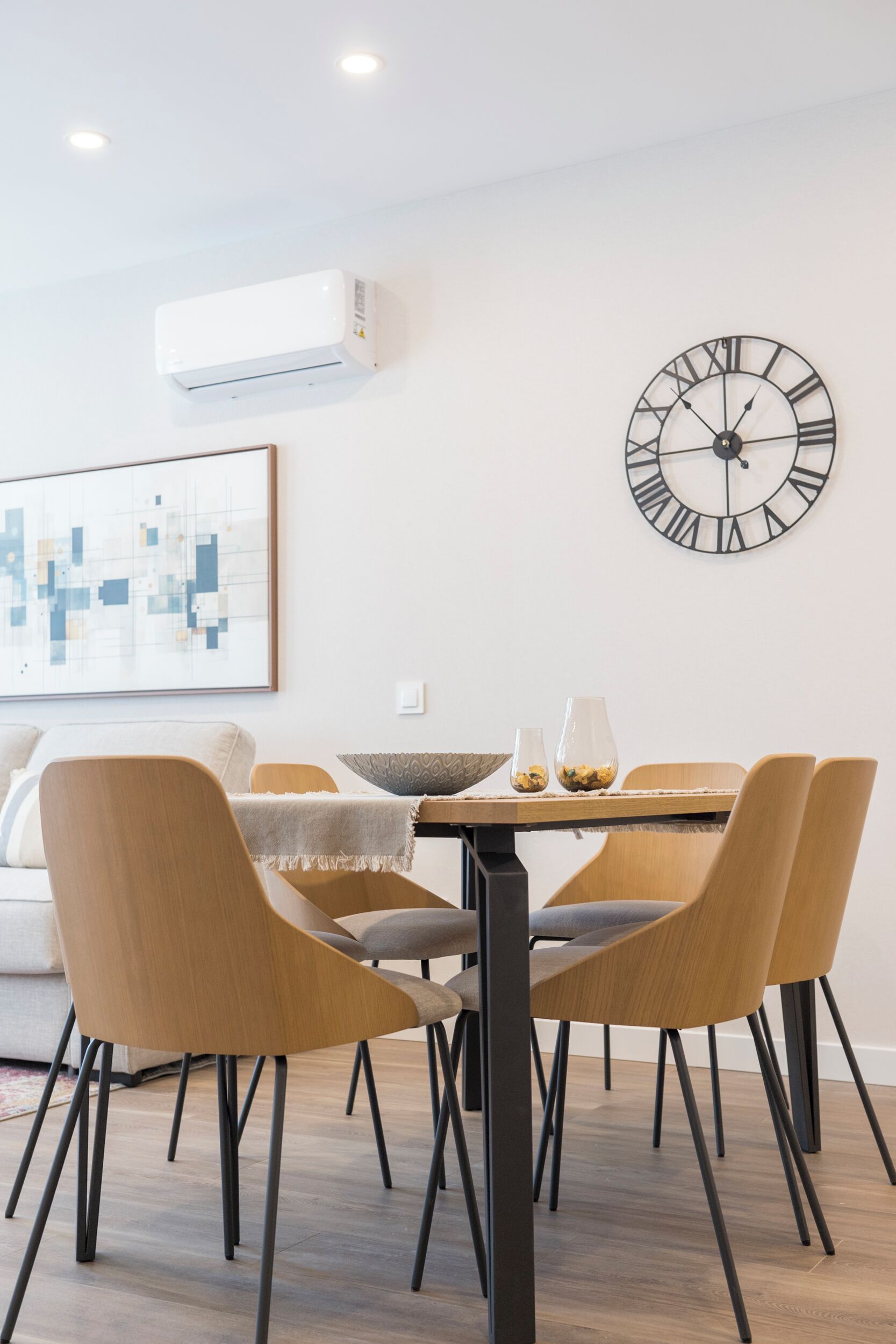 A dining area with a round table, six chairs, a wall clock, and an air conditioner.