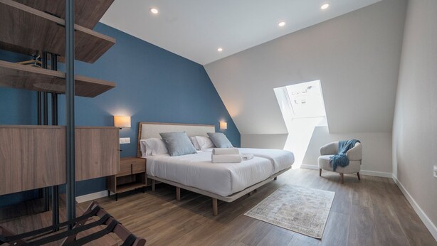 A bedroom with a bed, bedside tables, a chair, a desk, and a slanted ceiling. - Apartamentos Dúplex Príncipe de Canalejas (Madrid)