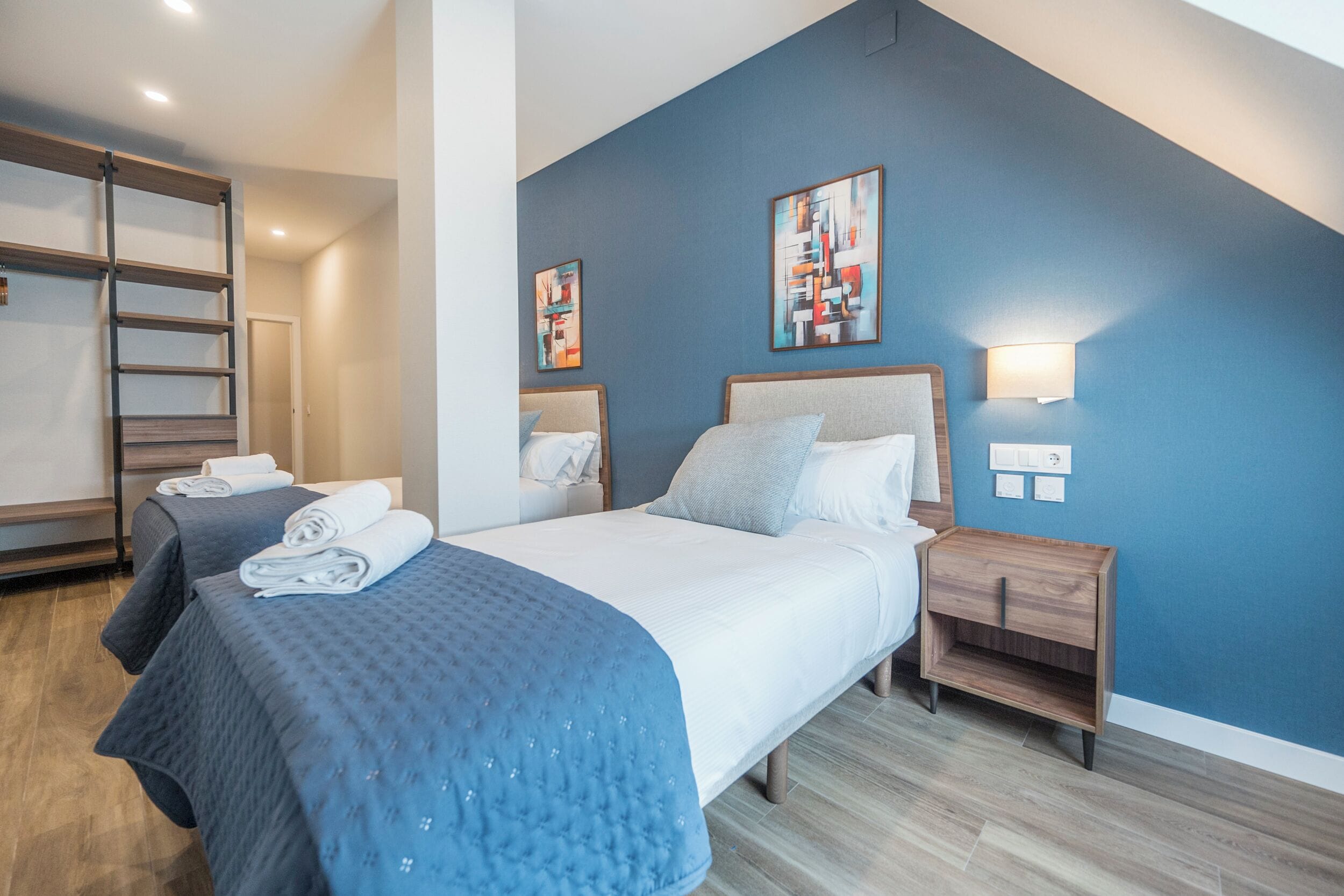 Una habitación de hotel con una cama, dos mesitas de noche, una lámpara de pared y una escalera.