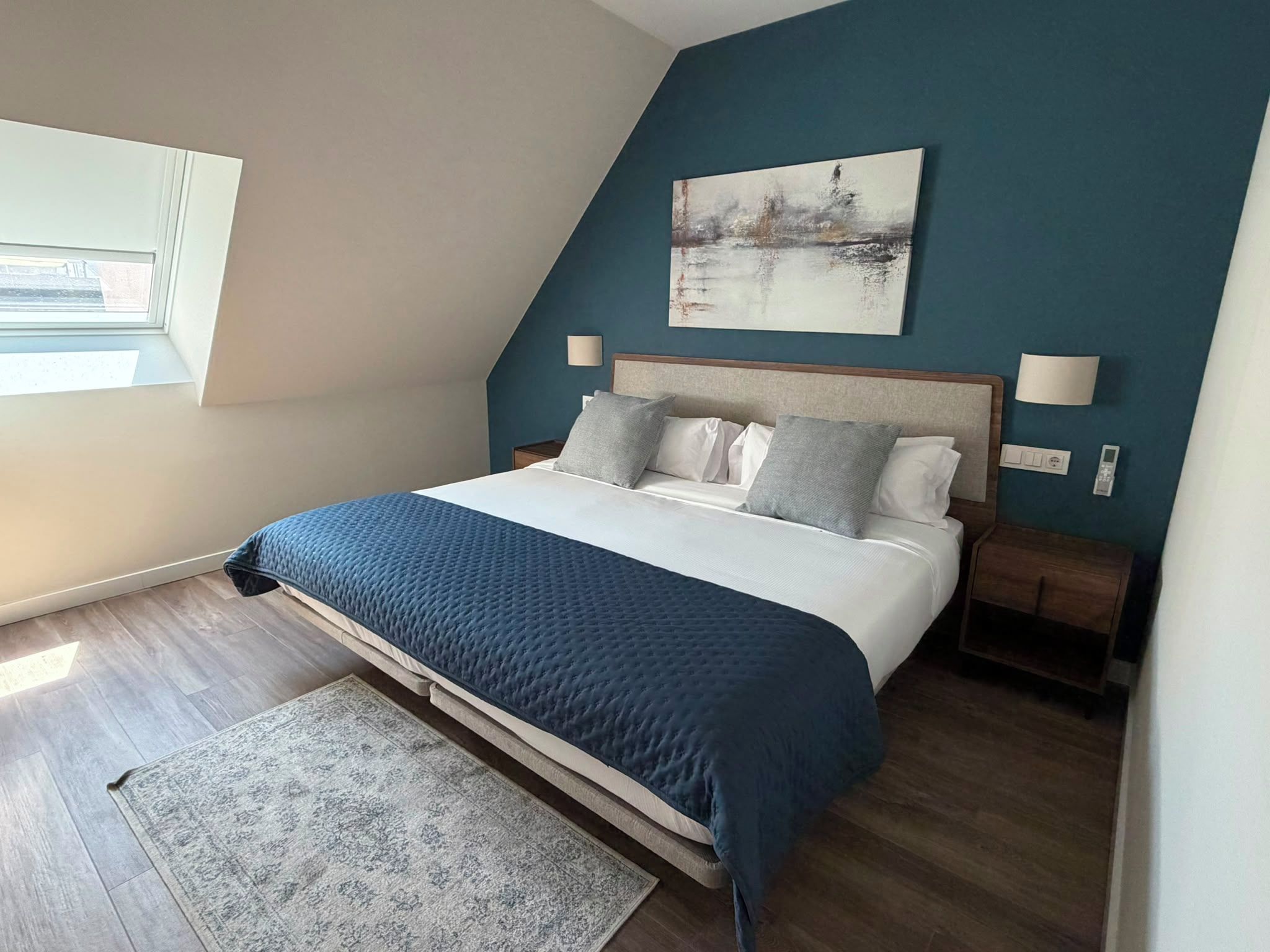 Un dormitorio moderno con una cama, mesitas de noche, una alfombra y un cuadro en la pared.