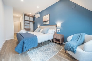 A bedroom with a bed, bedside tables, a nightstand, a chair, a ladder, a painting, and a blue wall. - Apartamentos Dúplex Príncipe de Canalejas (Madrid)