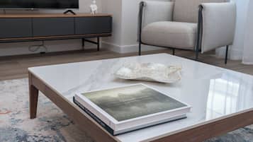 Una sala de estar moderna con una mesa de centro de vidrio, un libro, un televisor, un sofá gris y un mueble de madera.