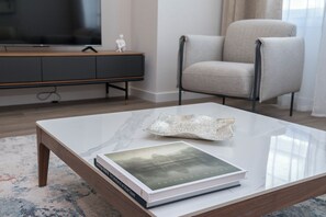 A modern living room with a glass coffee table, a book, a television, a grey sofa, and a wooden cabinet. - Apartamentos Dúplex Príncipe de Canalejas (Madrid)
