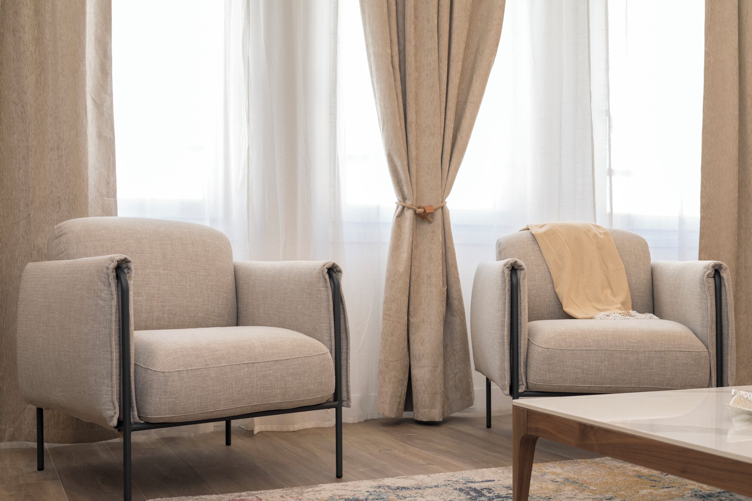 Two armchairs with a wooden coffee table in a room with a large window and sheer curtains.