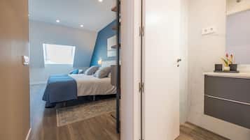 Un dormitorio moderno con cama, mesita de noche, ventana y baño con espejo y lavamanos.