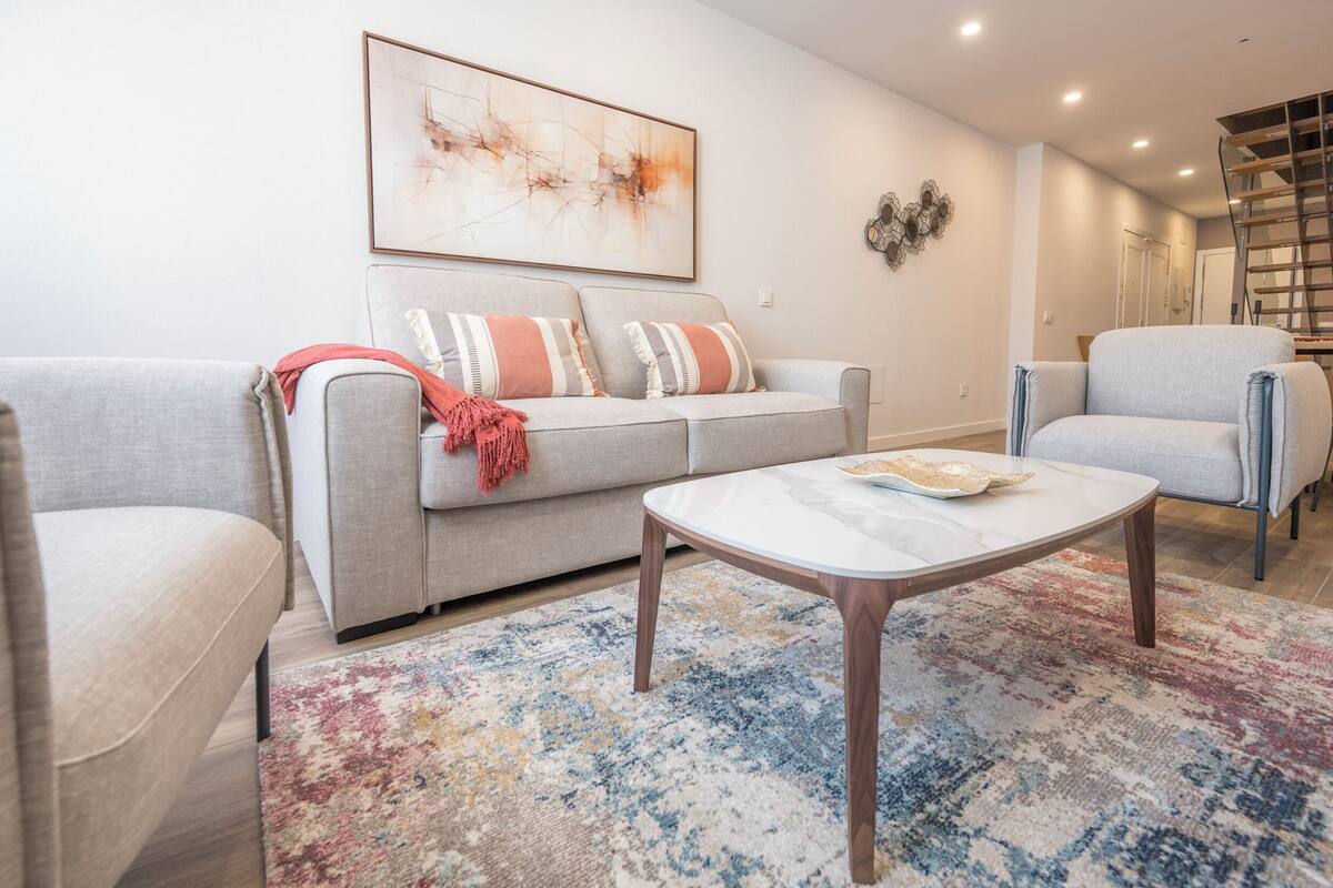 Una sala de estar con sofá, sillón, mesa de centro y una obra de arte abstracta en la pared.