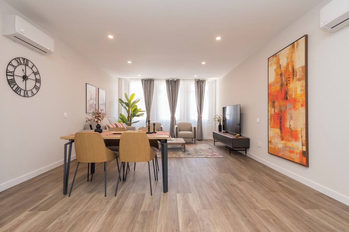 Una sala de estar moderna con comedor, televisor de pantalla plana y un cuadro abstracto grande.