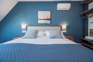 A bedroom with a bed, two bedside tables, a wall-mounted air conditioner, and a framed picture above the bed. - Dúplex Príncipe de Canalejas (Madrid)