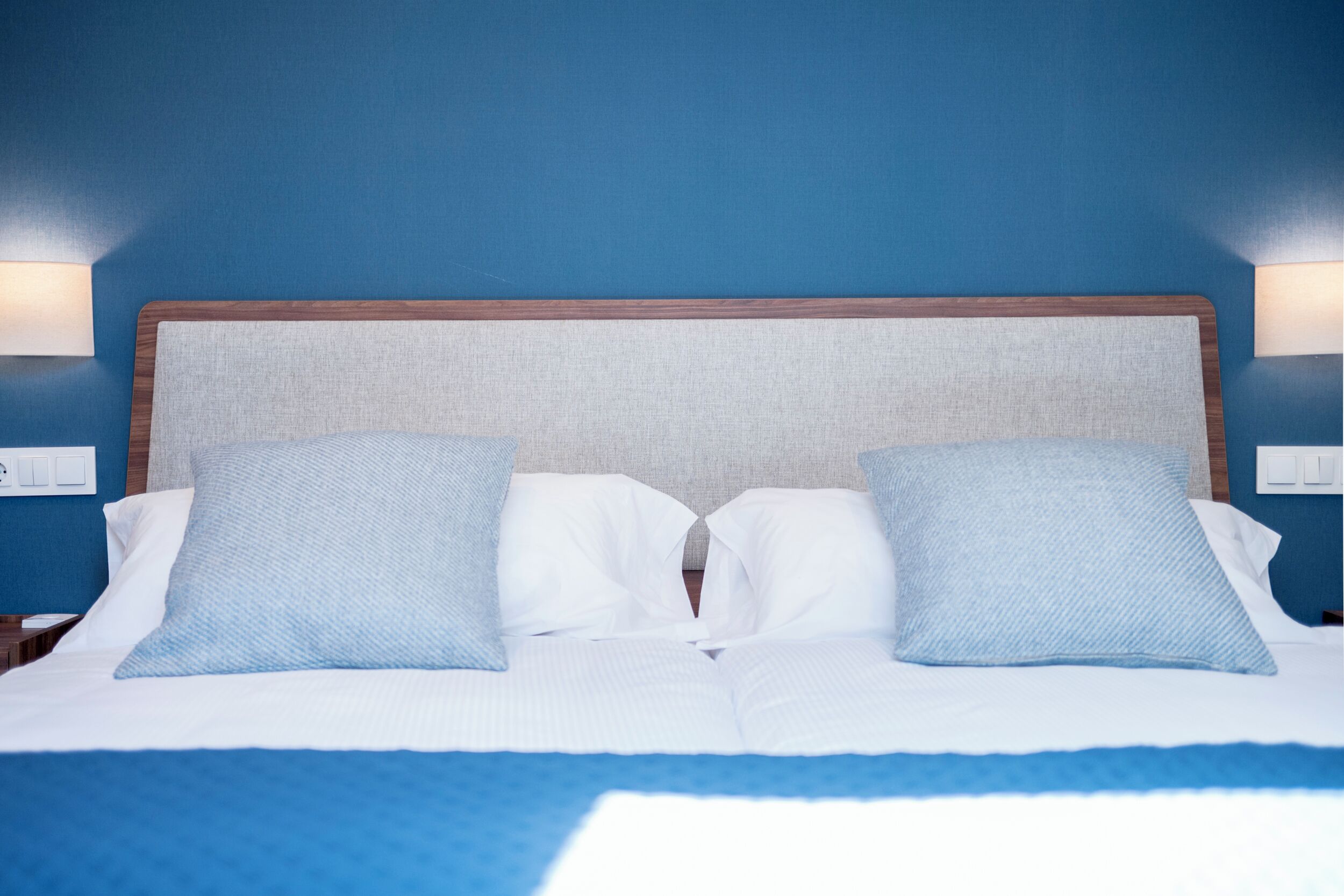 A bed with a headboard, two pillows, and a blue blanket.