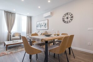 Ett modernt vardagsrum med en matplats, med ett träbord, grå klädda stolar, en beige soffa och en stor väggklocka.