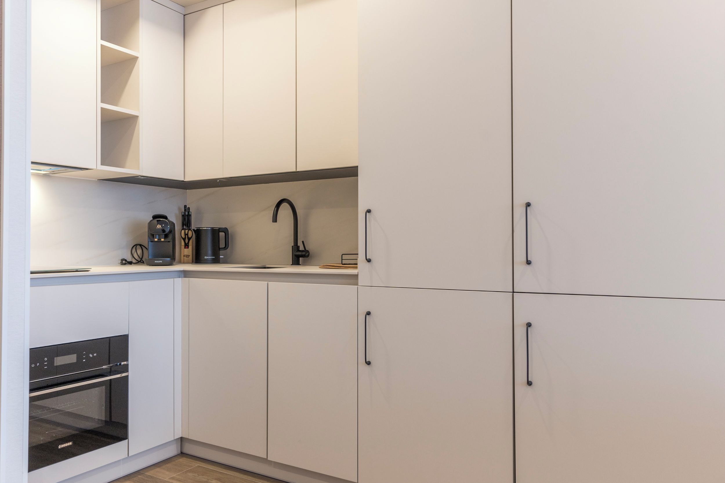 A modern kitchen with white cabinets, a built-in oven, and a coffee maker on the countertop.