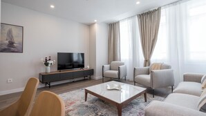 A modern living room with a flat-screen TV, a sofa, armchairs, a coffee table, and a painting on the wall. - Apartamentos Dúplex Príncipe de Canalejas (Madrid)