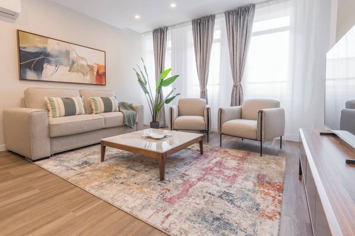 Una sala de estar con un sofá, sillones, una mesa de centro, una planta en maceta y un cuadro en la pared.