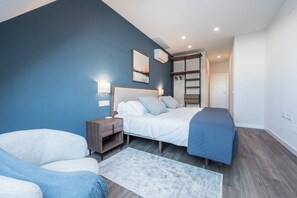 A bedroom with a bed, bedside tables, a chair, a blue wall, and a door leading to another room. - Dúplex Príncipe de Canalejas (Madrid)