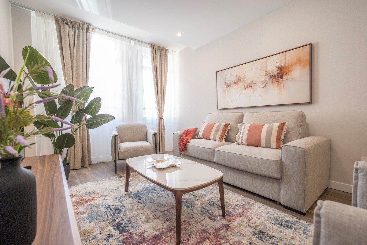 A living room with a sofa, armchairs, a coffee table, a large abstract painting, and a potted plant.