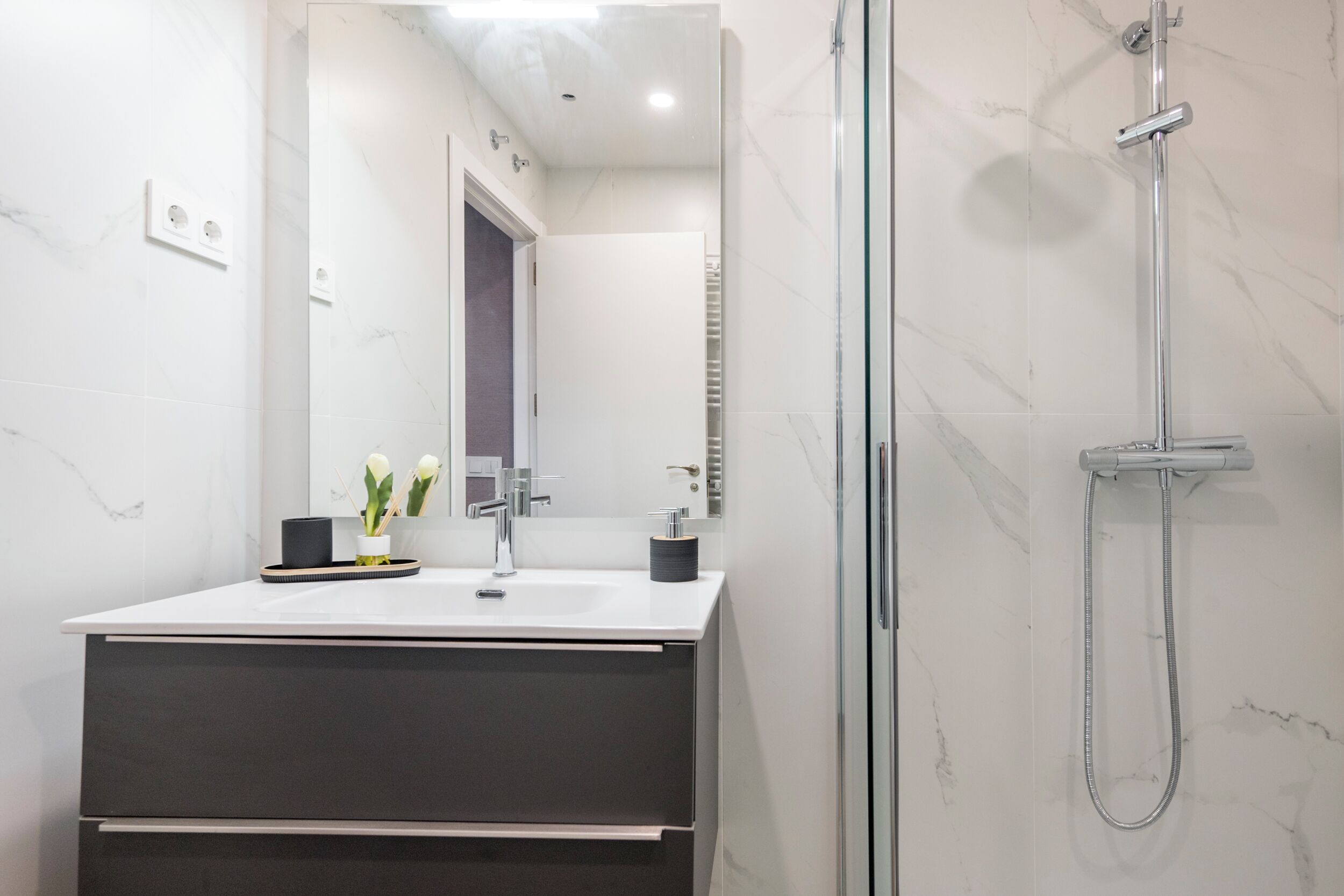 A modern bathroom with a glass-enclosed shower, a white sink with a dark countertop, and a mirror above the sink.