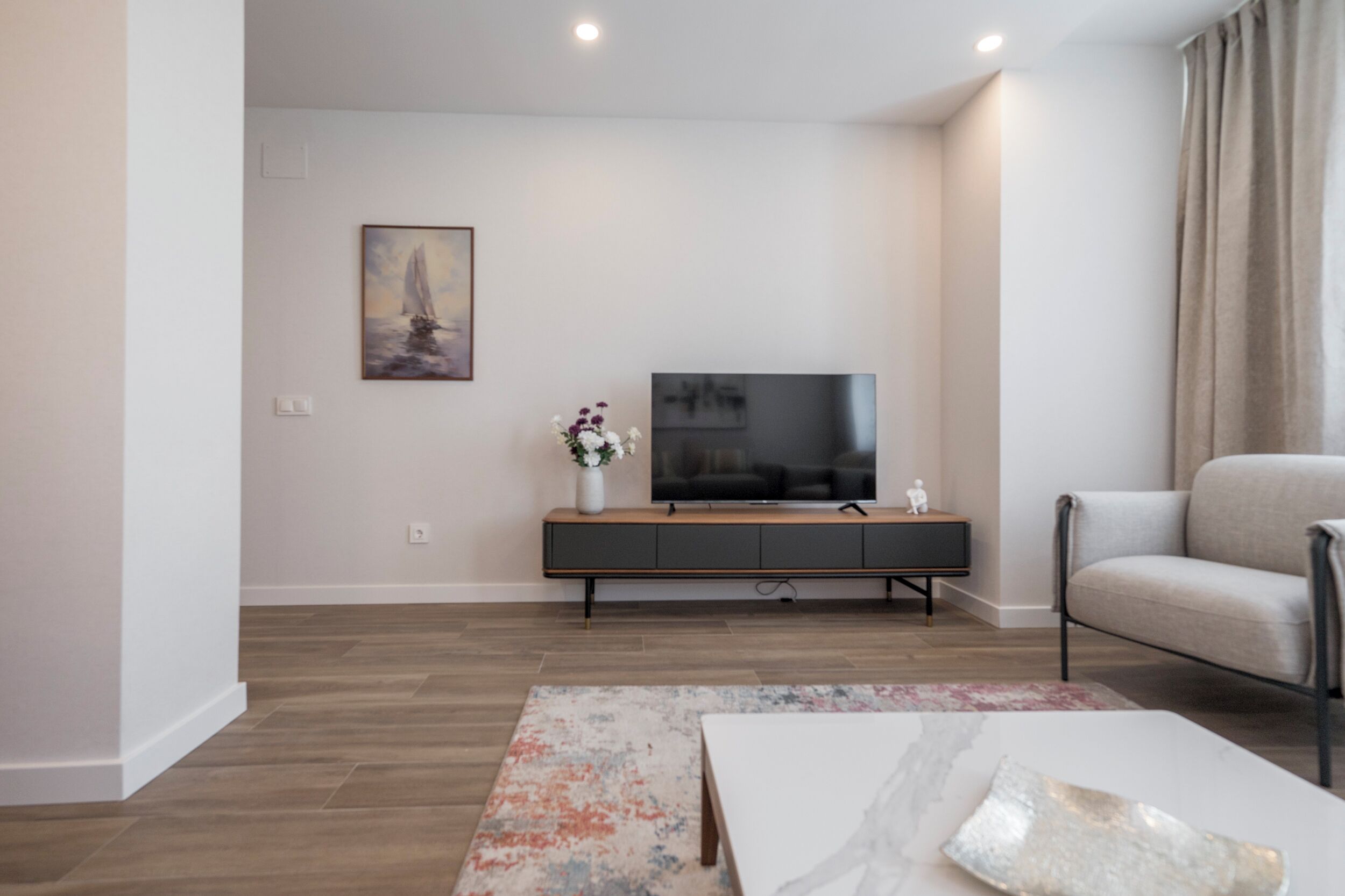 A modern living room with a flat-screen TV, a sofa, a coffee table, and a painting on the wall.