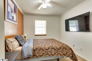 Een slaapkamer met een bed, een plafondventilator, een raam en een wandgemonteerde flatscreen-tv.