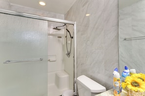 Un baño moderno con ducha envuelta en vidrio, inodoro blanco y pared de mármol.