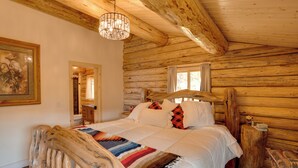 Ein Schlafzimmer in einer Blockhütte mit einem hölzernen Bett, einer Chandelüster und einem Gemälde an der Wand.