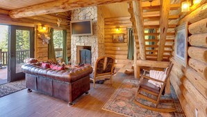 Ein Blockhaus-Interieur mit Kamin aus Stein, Ledersofa, Schaukelstuhl und Holzwänden.