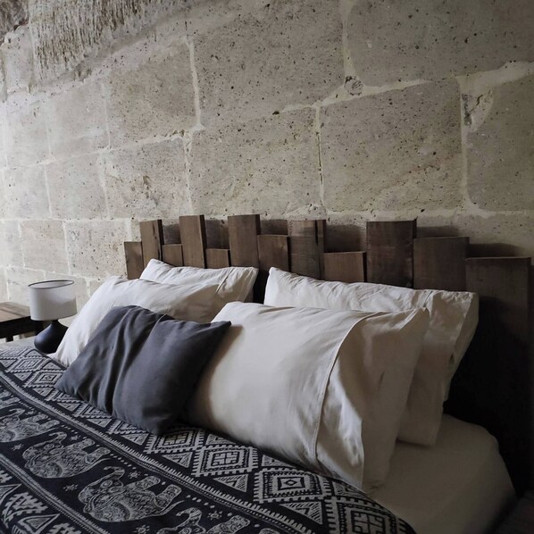 Una cama con una colcha estampada, un cabecero hecho de tablones de madera y una lámpara sobre una mesita de noche.