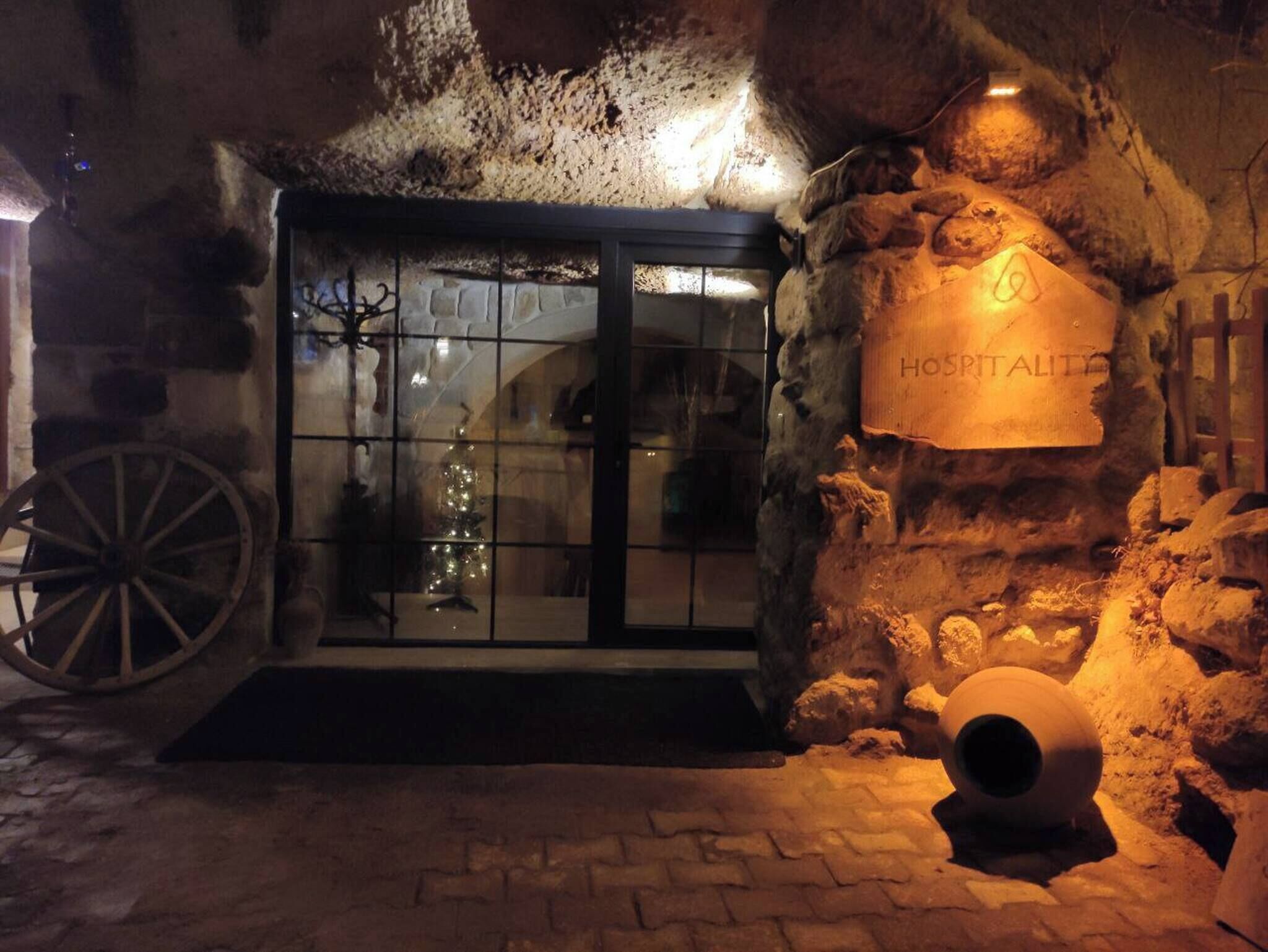 A rustic hotel entrance with a stone wall, a wooden sign reading 'HOTEL ALTO,' and a large wheel.