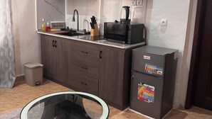 A compact kitchen with dark wood cabinets, a microwave, a refrigerator, and a glass bowl on a rug.