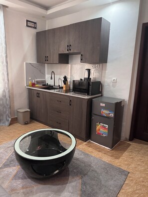 A compact kitchen with dark wood cabinets, a microwave, a refrigerator, and a glass bowl on a rug. - 5 minutes from downtown Kinshasa. Small, chic, modern apartment 2. (Kinshasa)