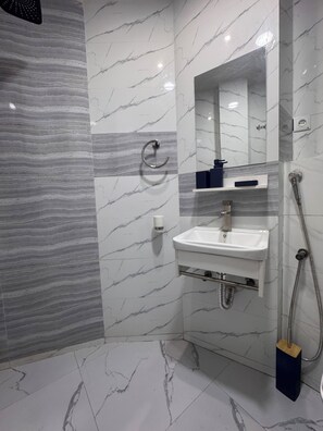 Un baño con pared de mármol, lavamanos, espejo, ducha y toallero.