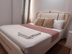 A neatly made bed with a white and pink bedspread, two leopard print pillows, and a folded white towel. - 5 minutes from downtown Kinshasa. Small, chic, modern apartment 2. (Kinshasa)