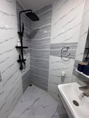 A bathroom with a shower, a sink, a towel ring, and a shelf with toiletries. - 5 minutes from downtown Kinshasa. Small, chic, modern apartment 2. (Kinshasa)