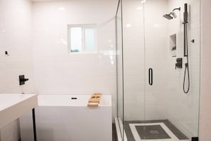 Ein modernes Badezimmer mit einer gläsernen Duschkabine, einer weißen Badewanne und einem kleinen Fenster darüber.