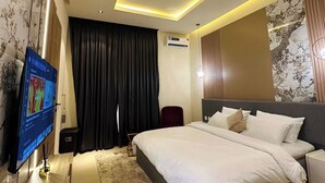 Habitación de hotel moderna con una cama grande, un televisor de pantalla plana, un equipo de aire acondicionado y un plafón.