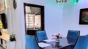 Un comedor con una mesa negra, sillas azules y un florero con flores rosadas.