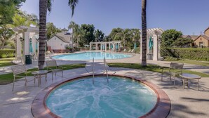 Un área de piscina con jacuzzi, sillas de descanso y una pérgola.