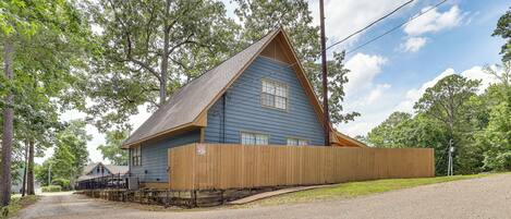 A blue building with a sloped roof, a wooden fence, and a gravel driveway.