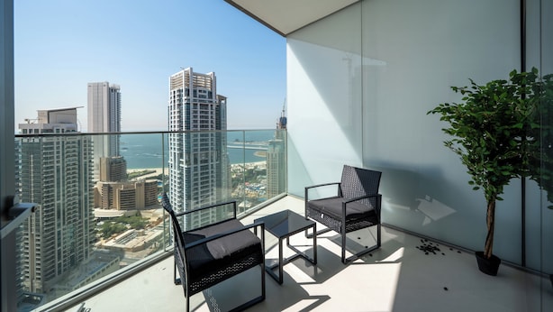 A balcony with two chairs and a table, a potted plant, and a view of a cityscape and water. - Premium Skyline 1BR with Sea View LIV Marina (Dubai)