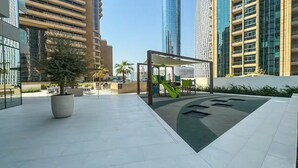 A modern outdoor area with a children's play structure, seating, and a large planter. - Premium Skyline 1BR with Sea View LIV Marina (Dubai)