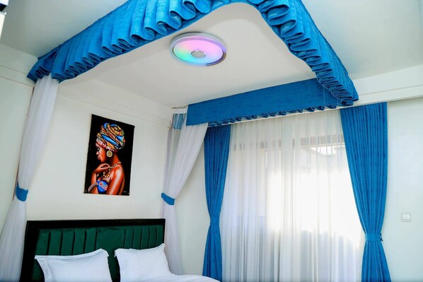 A room with a bed, a ceiling light, a painting, and blue curtains. - Cozy 2bed master-ensuite apt in Nairobi near the Airport and SGR train station (Nairobi)